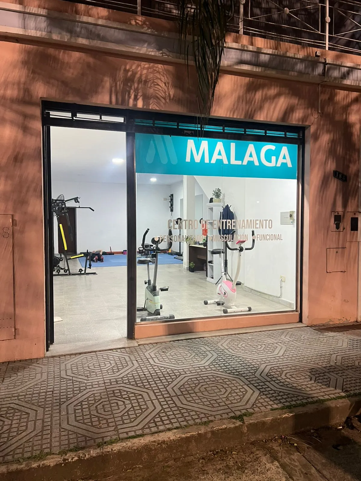 Frente del local de Málaga de noche, con el cartel turquesa iluminado