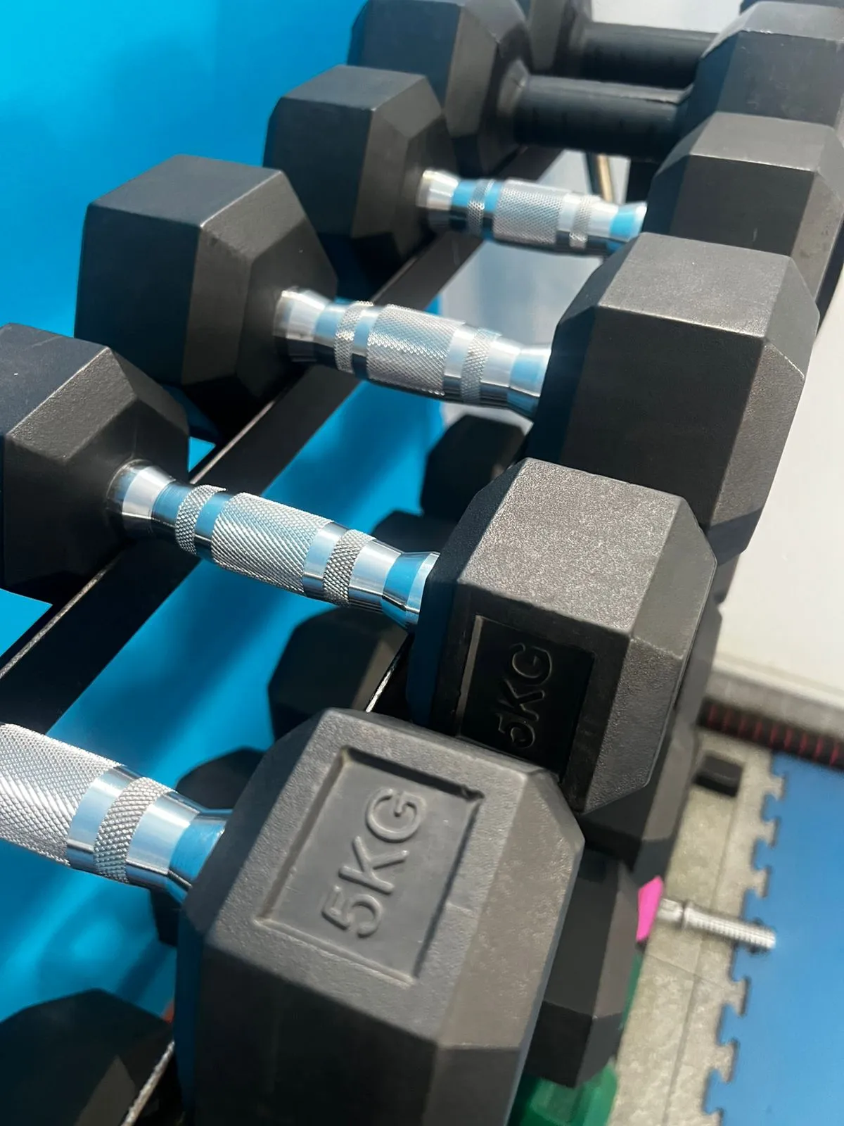 Mancuernas hexagonales de 5 kg en el rack, con detalle turquesa
